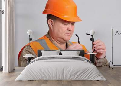 face of engineer in hard hat putting on protective glasses on grey background, safety at building work Wall mural