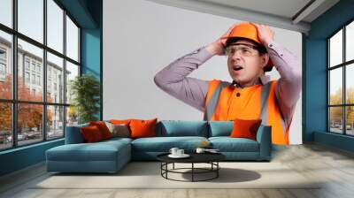 young engineer architect clutching his head in helmet on grey studio background, foreman shocked Wall mural