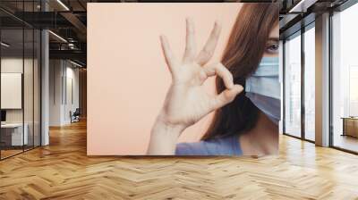 young woman wearing a protective mask on face and showing gesture ok with suspect, concept health control, obedience quarantine measures Wall mural