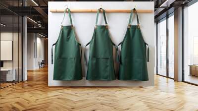 Three dark green waterproof thick canvas aprons hanging on a wooden crossbar on a white wall Wall mural