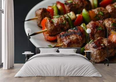 A close-up shot of meat kebabs on a white plate, with green and red peppers as garnish. The dish is set against a black background to highlight its vibrant colors. Wall mural