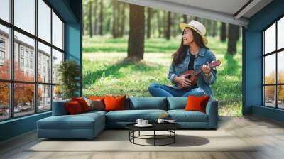 A beautiful asian woman sitting and playing ukulele in the park Wall mural