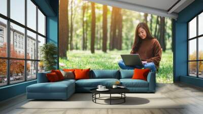 A beautiful asian woman working and typing on laptop keyboard while sitting in the park Wall mural