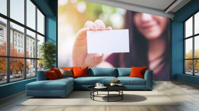 A beautiful woman holding and showing empty business card with smiley face in nature background Wall mural