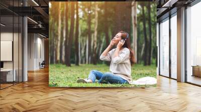 A beautiful young asian woman enjoy listening to music with headphone with feeling happy and relaxed in the park Wall mural