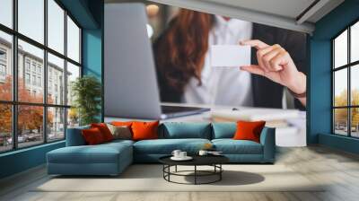 A businesswoman holding and showing a blank business cards while using laptop computer in office Wall mural