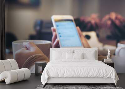 A woman's hands holding white coffee cup and mobile phone while using social media in modern loft cafe Wall mural