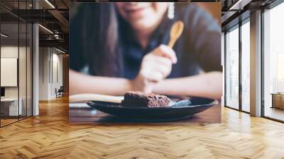 A woman eating and looking at brownie in black ceramic plate on wooden table with wooden spoon Wall mural