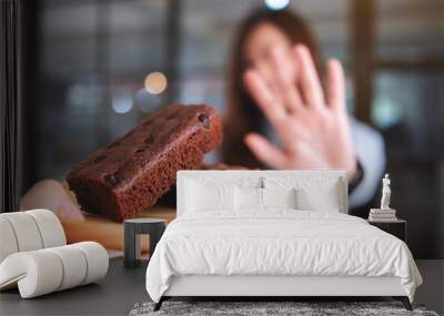 A woman making hand sign to refuse a brownie cake in wooden plate from someone Wall mural