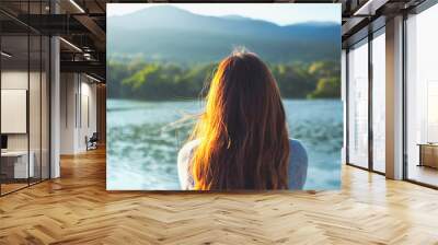 A woman sitting alone by the lake looking at the mountains with green nature background Wall mural