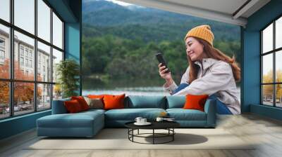 A young asian woman holding and using mobile phone while traveling mountains and lake Wall mural