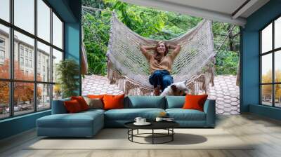 A young asian woman lying and relaxing on hammock with a dog sitting nearby Wall mural