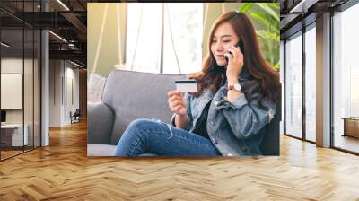 An asian woman using credit card for purchasing and shopping online while talking on mobile phone Wall mural