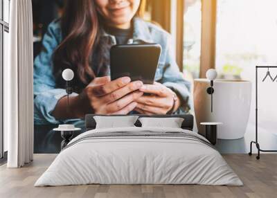 Closeup image of a beautiful asian woman holding and using mobile phone with coffee cup on the table Wall mural