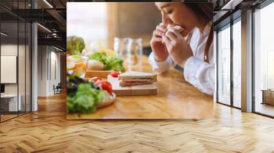 Closeup image of a female chef cooking and eating a whole wheat sandwich in kitchen Wall mural