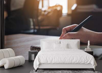 Closeup image of a hand writing down on a white blank notebook on wooden table Wall mural