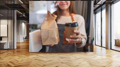 Closeup image of a waitress holding and serving paper cup of coffee and takeaway food in paper bag to customer in a shop Wall mural