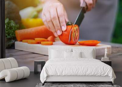 Closeup image of a woman cutting and chopping tomato by knife on wooden board Wall mural