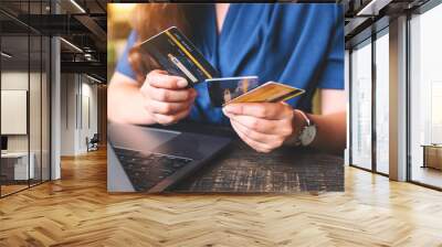 Closeup image of a woman holding and choosing credit cards while using laptop computer Wall mural