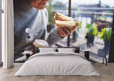 Closeup image of a woman holding and eating whole wheat sandwich and coffee in the morning Wall mural