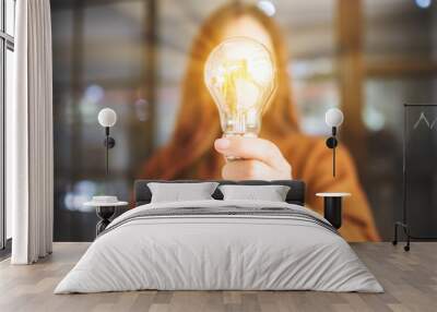 Closeup image of a woman holding and showing a glowing light bulb Wall mural