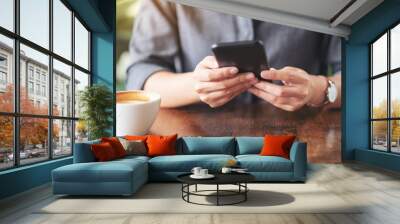 Closeup image of a woman holding  and using mobile phone with coffee cup on wooden table in cafe Wall mural