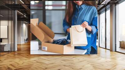 Closeup image of a woman opening and looking inside shopping bag with postal parcel box of clothing for delivery and online shopping concept Wall mural