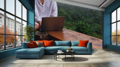 Closeup image of a woman using and working on laptop computer while sitting on balcony with a beautiful nature view on foggy day Wall mural