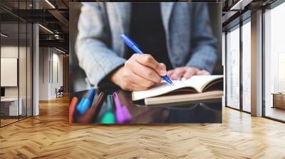 Closeup image of a woman writing on a blank notebook with colored pens on the table Wall mural