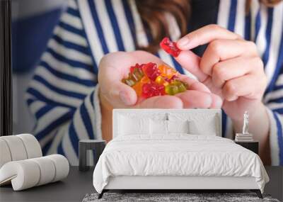 Closeup image of a young woman holding and eating jelly gummy bears Wall mural