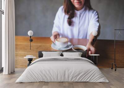 Closeup image of a young woman holding and serving two cups of hot coffee Wall mural