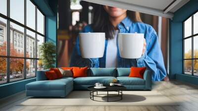 Closeup image of a young woman holding and serving two cups of hot coffee Wall mural