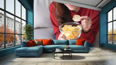 Closeup image of a young woman picking and eating potato chips at home Wall mural