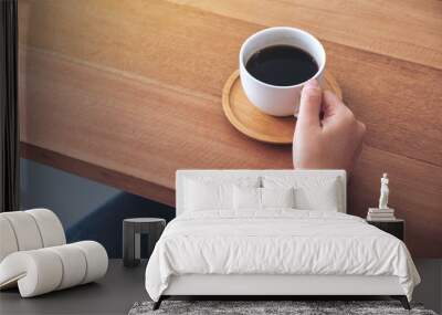 Closeup image of hand holding a white cup of hot coffee to drink on wooden table Wall mural