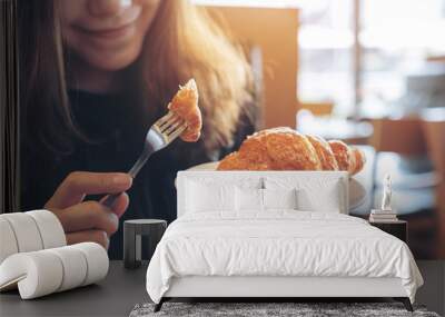 Closeup image of hands cutting a piece of croissant by fork to eat on wooden table Wall mural