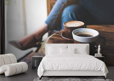 Closeup image of two cups of hot latte coffee on vintage wooden table with woman sitting in background Wall mural