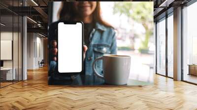 Mockup image of a beautiful woman holding and showing black mobile phone with blank screen in cafe Wall mural