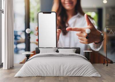 Mockup image of a beautiful woman pointing finger at a mobile phone with blank white screen Wall mural