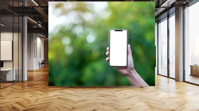 Mockup image of a hand holding black mobile phone with blank desktop screen with green nature background Wall mural