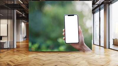 Mockup image of a hand holding black mobile phone with blank desktop screen with green nature background Wall mural