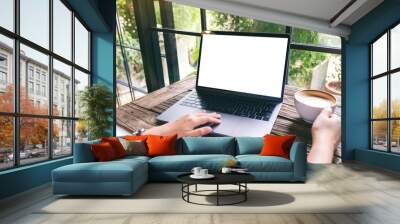 Mockup image of a hand using and touching on laptop touchpad with blank white desktop screen while drinking coffee Wall mural