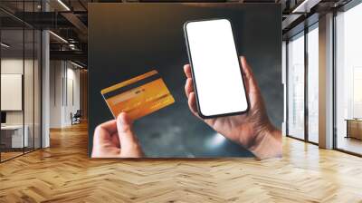 Mockup image of a hands holding credit card and a black mobile phone with blank desktop screen Wall mural