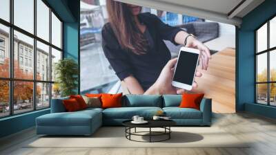 Mockup image of a man's hand holding and giving white mobile phone with blank black screen to a woman in cafe Wall mural