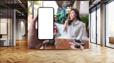 Mockup image of a man's hand holding black mobile phone with blank white screen with woman sitting in cafe Wall mural