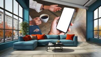 Mockup image of a man holding and showing mobile phone with blank  desktop screen to his friend while having conversation together Wall mural