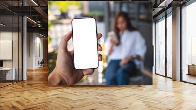 Mockup image of a man holding mobile phone with blank white screen with a woman in background Wall mural