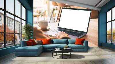 Mockup image of a woman's hand using and touching on laptop touchpad with blank white desktop screen with coffee cup on wooden table Wall mural