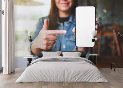 Mockup image of a woman holding, showing and pointing finger at a mobile phone with blank white screen Wall mural