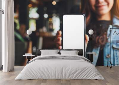 Mockup image of a woman holding and showing black mobile phone with blank white screen in cafe Wall mural