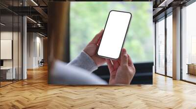 Mockup image of a woman holding and using mobile phone with blank desktop white screen at home Wall mural